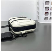 Borsa a tracolla bianca e nera su tavolo grigio, design moderno e compatto, ideale per uomo e donna, accessorio moda unisex.