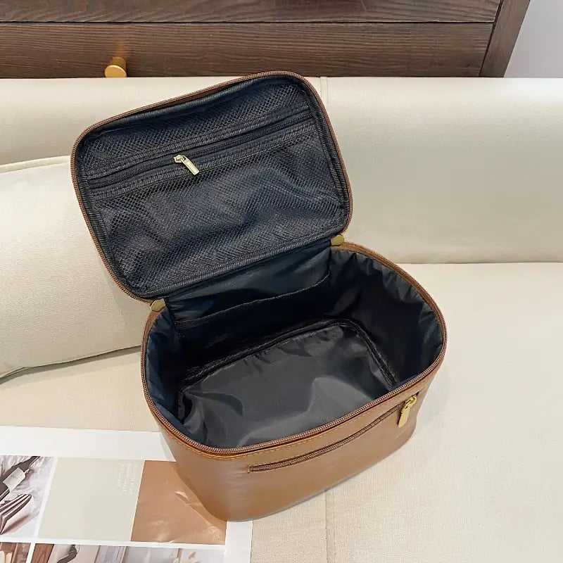 Borsa organizer da viaggio marrone aperta su divano beige, con tasca interna a rete e cerniera dorata. Ideale per cosmetici e accessori.