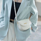 Giacca elegante azzurra su donna con borsa a tracolla bianca in pelle, abbinata a top nero e pantaloni chiari. Moda femminile chic e moderna.