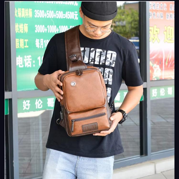 Uomo con borsa a tracolla in pelle marrone, indossa cappello nero e occhiali. Moda casual, esterno negozio. Accessorio maschile trendy.