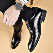 Scarpe eleganti uomo in pelle nera lucida, indossate con calzini neri e pantaloni a righe. Orologio da polso classico in vista.