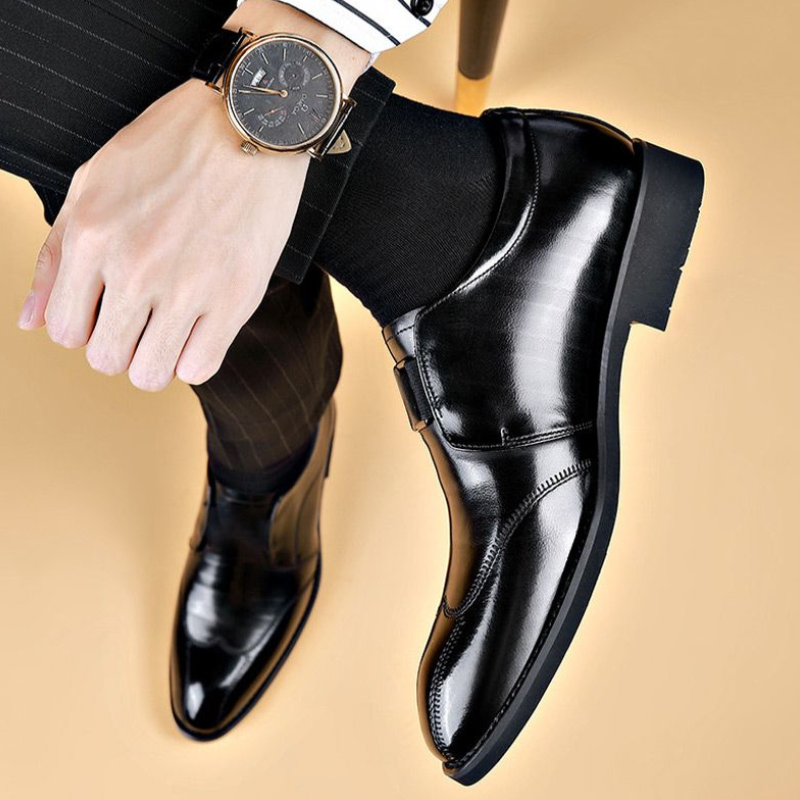Scarpe eleganti uomo in pelle nera lucida, indossate con calzini neri e pantaloni a righe. Orologio da polso classico in vista.