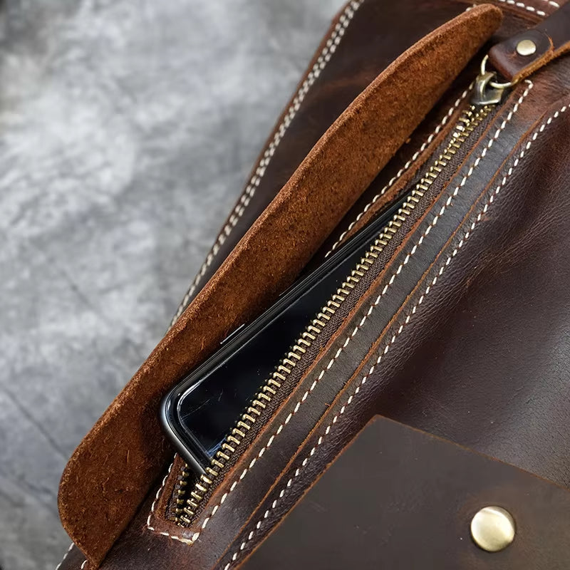 Borsa in pelle marrone con cerniera dorata, cuciture bianche e tasca interna contenente uno smartphone. Accessorio moda elegante e funzionale.
