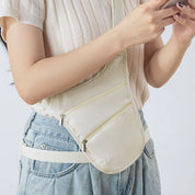 Donna con marsupio bianco a tracolla, indossa jeans e maglietta bianca, utilizza smartphone. Accessorio moda casual, pratico per viaggi e passeggiate.