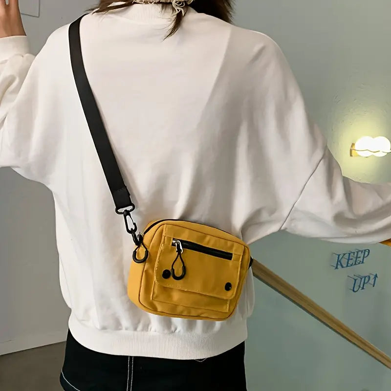Borsa a tracolla gialla unisex, design compatto, con tasche frontali e cerniera, indossata su felpa bianca. Accessorio moda casual.