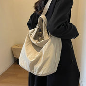 Borsa a tracolla beige in tessuto morbido, indossata da una persona con cappotto nero. Design casual ed elegante, ideale per l'uso quotidiano.