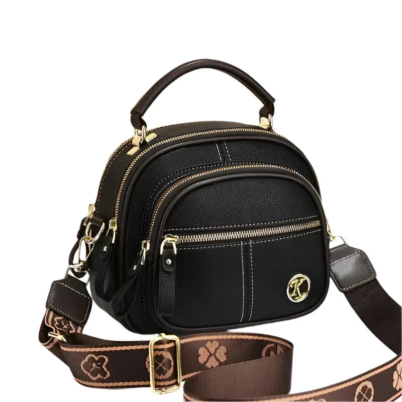 Borsa a tracolla in pelle nera con dettagli dorati, manico superiore, cerniere multiple e tracolla regolabile marrone con motivo floreale.