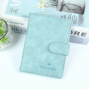 Custodia passaporto in pelle azzurra su tavolo bianco, accanto a libro e pianta. Design elegante, ideale per viaggiatori. Accessorio viaggio essenziale.