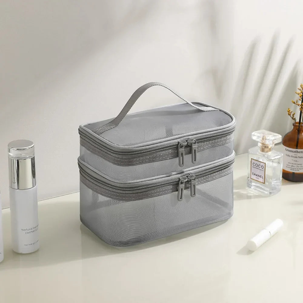 Borsa da toilette grigia a due scomparti con cerniera, manico superiore, su tavolo con profumo e cosmetici. Organizzatore da viaggio elegante.