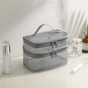 Borsa da toilette grigia a due scomparti con cerniera, manico superiore, su tavolo con profumo e cosmetici. Organizzatore da viaggio elegante.
