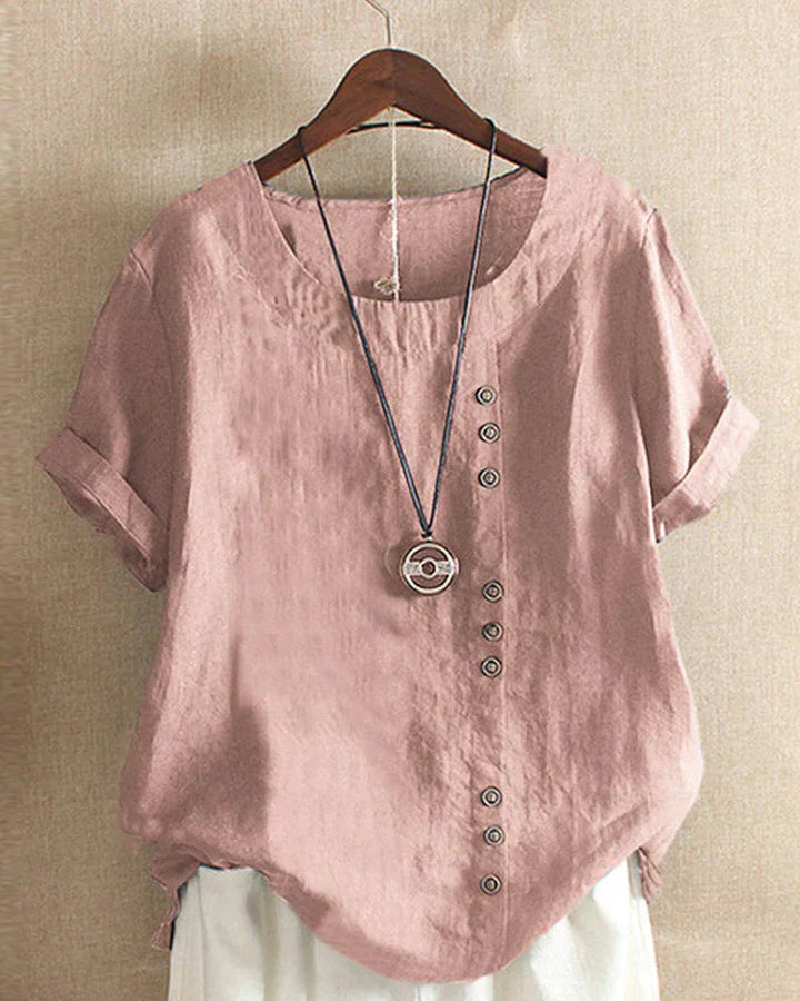 Blusa donna in lino rosa con bottoni decorativi, maniche corte risvolte, scollo rotondo, abbinata a collana pendente. Stile casual elegante.