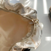 Borsa in tessuto beige con cerniera dorata e dettaglio perla, design elegante e raffinato, perfetta per moda femminile e accessori di tendenza.