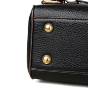 Borsa in pelle nera con dettagli in metallo dorato, texture granulosa, design elegante e moderno, perfetta per moda e accessori di lusso.