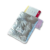 Porta passaporto argentato con motivo a fiocco, contenente biglietti aerei colorati. Accessorio da viaggio elegante e funzionale.