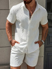 Uomo con completo estivo bianco in tessuto lavorato, camicia a maniche corte e pantaloncini coordinati. Look casual elegante per moda maschile estiva.