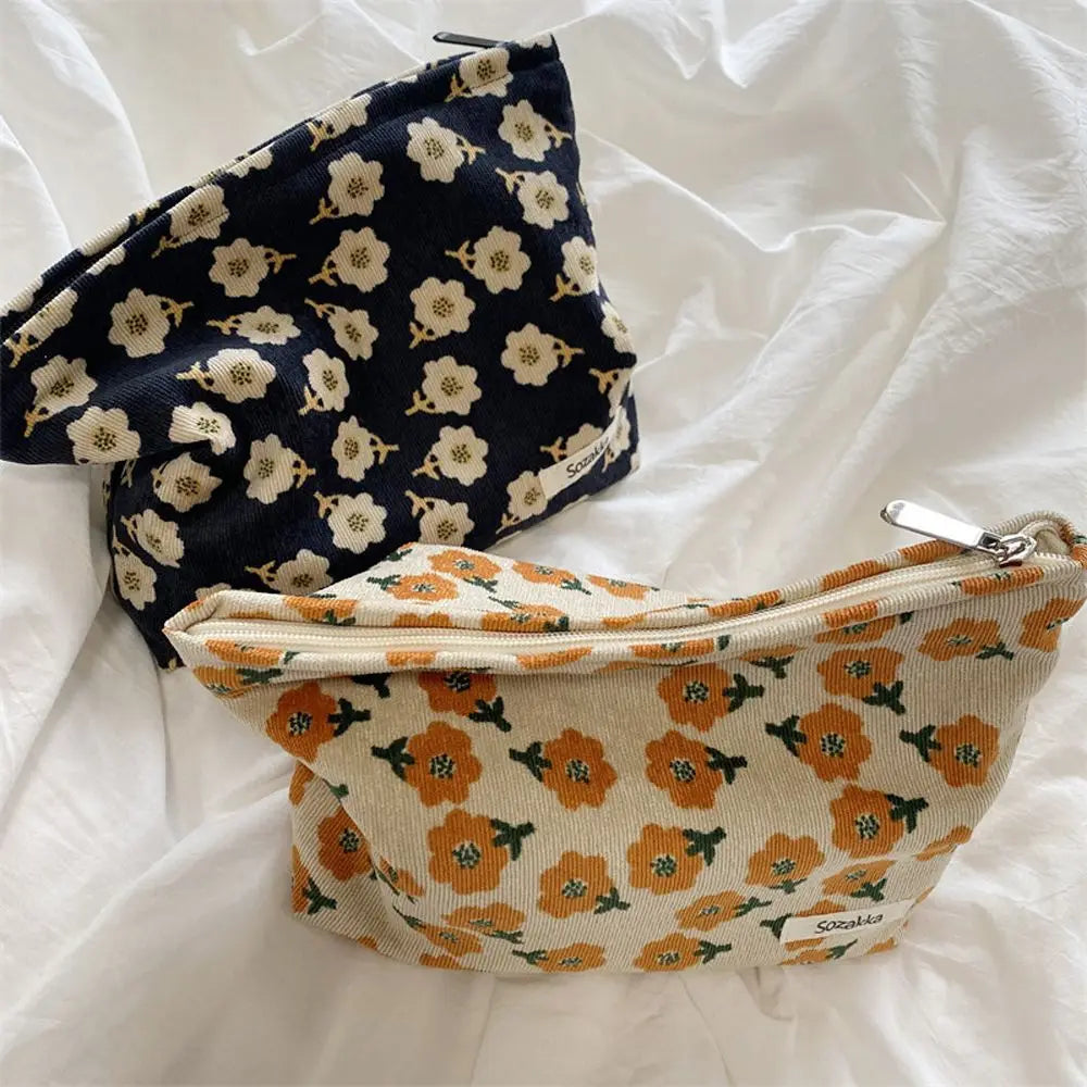 Due pochette in tessuto floreale, una blu con fiori bianchi e una beige con fiori arancioni, su sfondo bianco. Accessori moda eleganti e pratici.