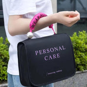 Borsa nera per trucco con scritta "Personal Care", manico rosa con perla, indossata al polso. Ideale per organizzare cosmetici e accessori.