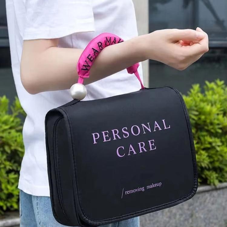 Borsa nera per trucco con scritta "Personal Care", manico rosa con perla, indossata al polso. Ideale per organizzare cosmetici e accessori.