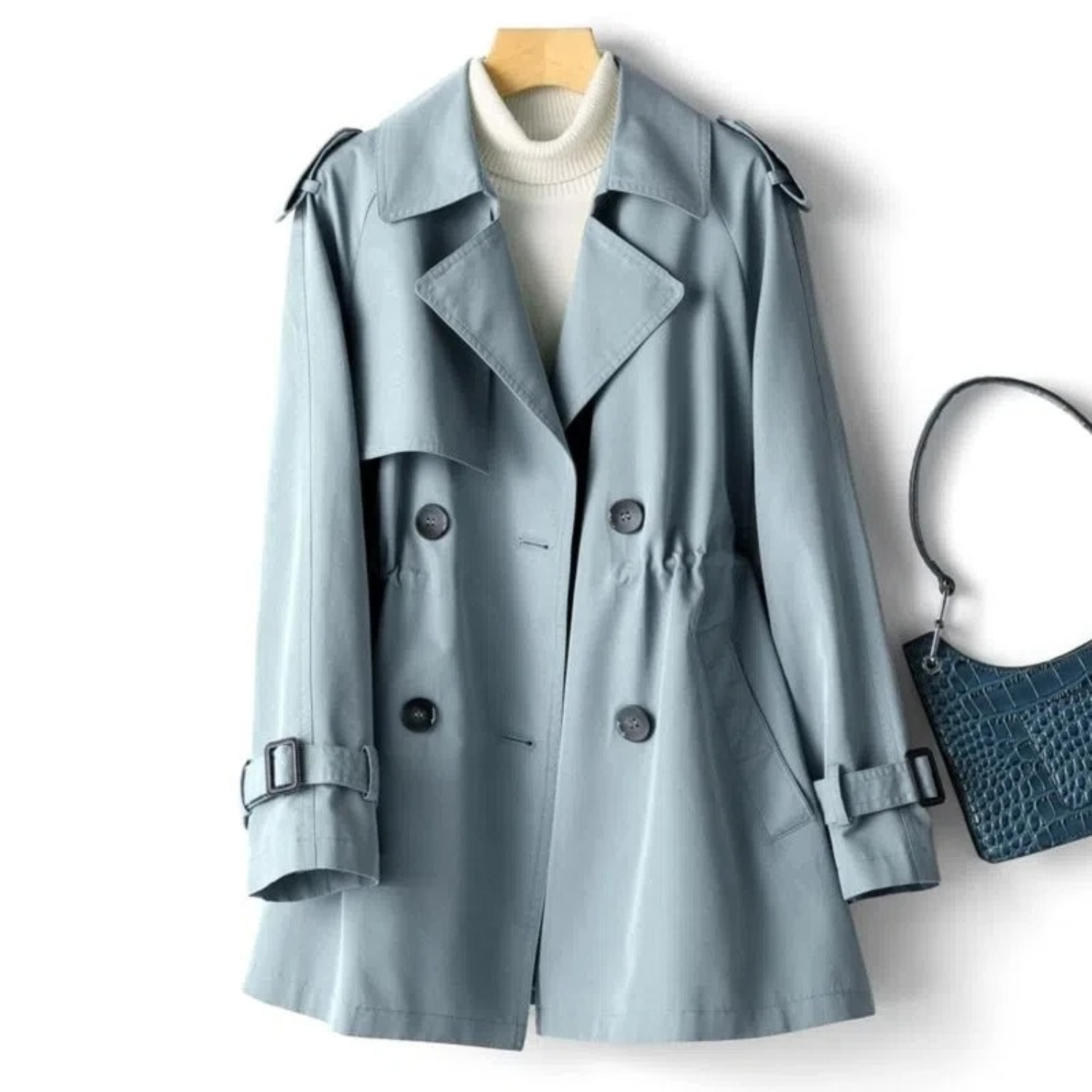 Cappotto trench donna azzurro, doppio petto, con cintura e tasche, abbinato a borsa blu in pelle. Elegante e versatile per l'autunno.