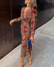 Donna con abito lungo rosso a fantasia floreale, sandali dorati e pochette blu. Moda elegante, abbigliamento femminile autunnale, stile sofisticato.