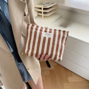 Borsa a righe marroni e bianche in tessuto, tenuta in mano da una persona in giacca beige. Design moderno, ideale per moda casual e accessori.