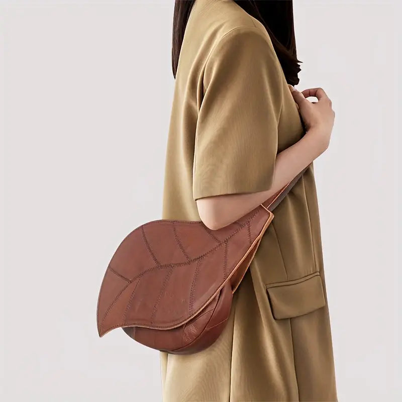 Borsa a tracolla a forma di foglia in pelle marrone, indossata da una donna con abito beige. Design unico, accessorio moda elegante.