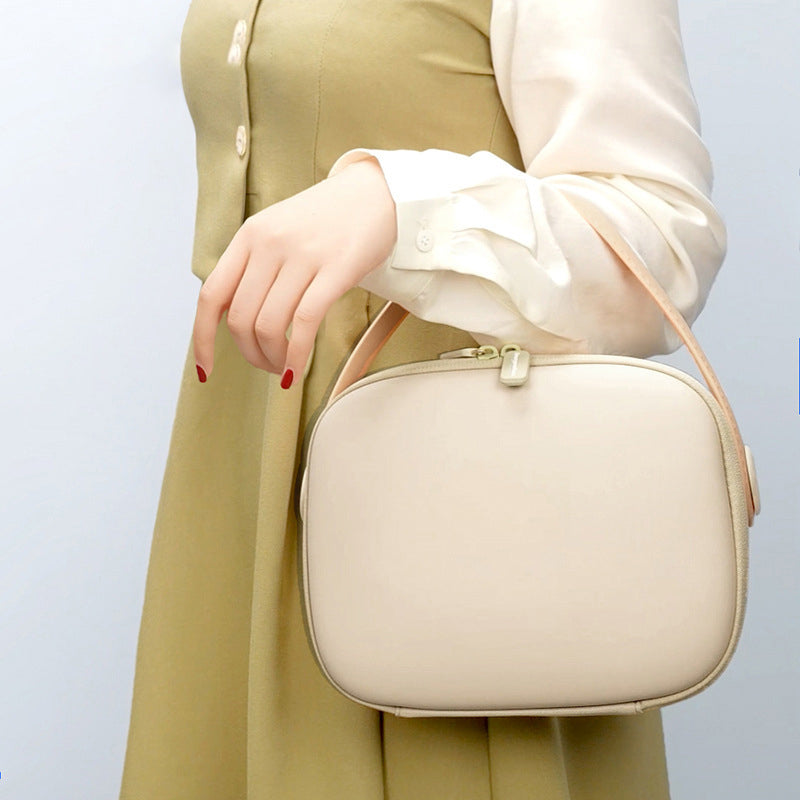 Borsa a tracolla beige elegante, indossata da una donna con abito verde chiaro e camicia bianca. Accessorio moda femminile chic e versatile.