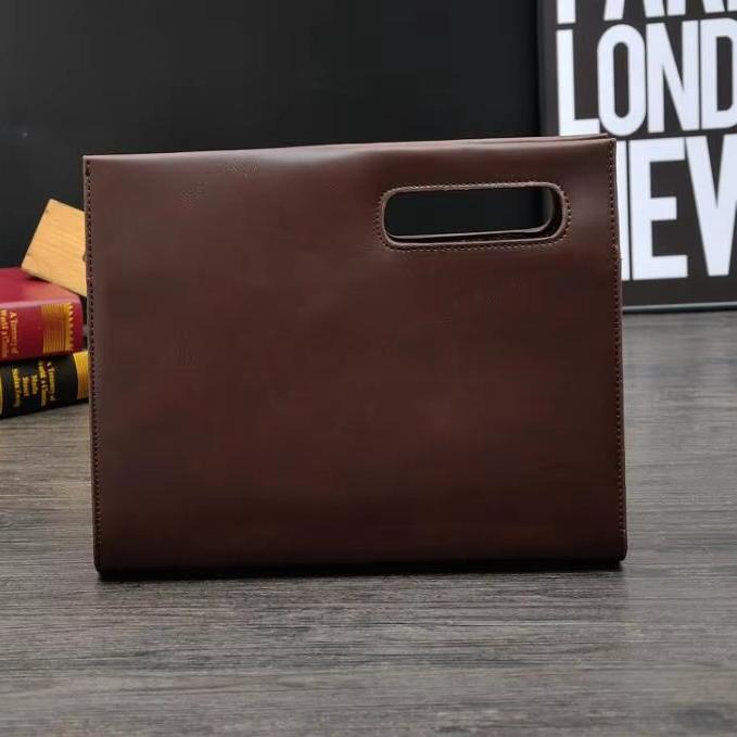 Borsa a mano in pelle marrone su tavolo di legno, design elegante e moderno, ideale per ufficio o viaggio. Sfondo con libri e poster.