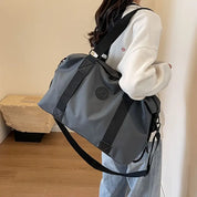 Donna con borsa da viaggio grigia e nera, tracolla regolabile, indossa felpa bianca e jeans. Accessorio moda, capiente e versatile.