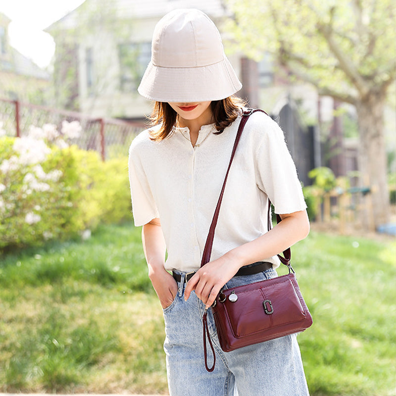 Donna con cappello beige, maglia bianca e jeans, indossa borsa a tracolla bordeaux. Moda casual estiva, accessori eleganti per passeggiate all'aperto.