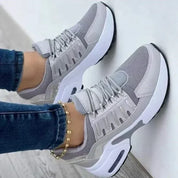 Scarpe da ginnastica grigie da donna, design moderno, suola ammortizzata, indossate con jeans. Sneakers casual per sport e tempo libero.