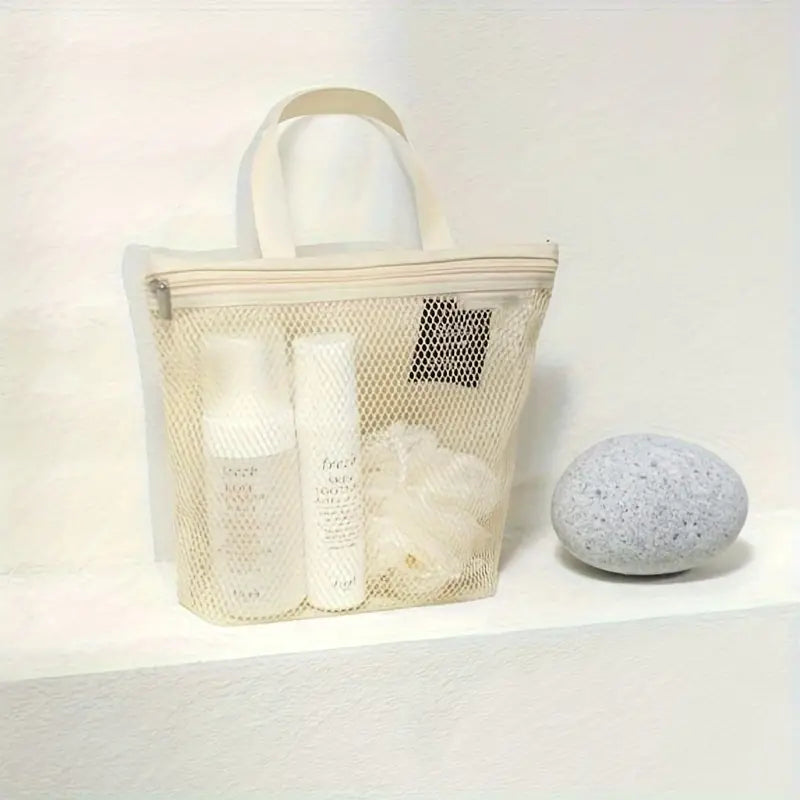 Borsa trasparente in rete con prodotti per la cura della pelle, flaconi bianchi e spugna, su sfondo bianco. Accessori da bagno eleganti e pratici.