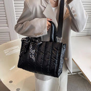 Borsa a tracolla nera trapuntata in nylon, indossata da una persona con giacca beige. Accessorio moda elegante, perfetto per l'autunno.