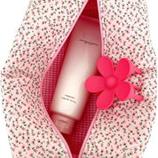 Borsa trucco rosa con motivo floreale, contenente un flacone di crema e un accessorio a forma di fiore. Accessori bellezza, cosmetici viaggio.