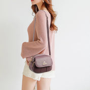 Donna con borsa a tracolla marrone, maglione rosa e shorts bianchi. Accessorio moda elegante, perfetto per look casual e chic.