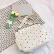 Borsa a tracolla floreale su tovaglia a quadri, accanto a fiori gialli e rosa in vaso di vetro. Design elegante, perfetto per moda casual.