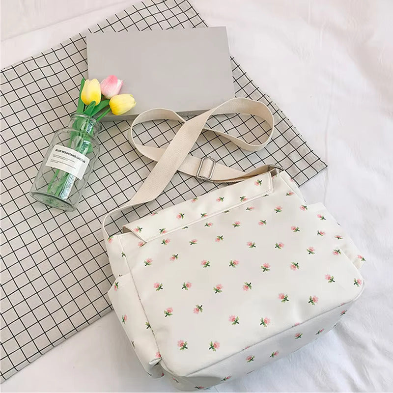 Borsa a tracolla floreale su tovaglia a quadri, accanto a fiori gialli e rosa in vaso di vetro. Design elegante, perfetto per moda casual.