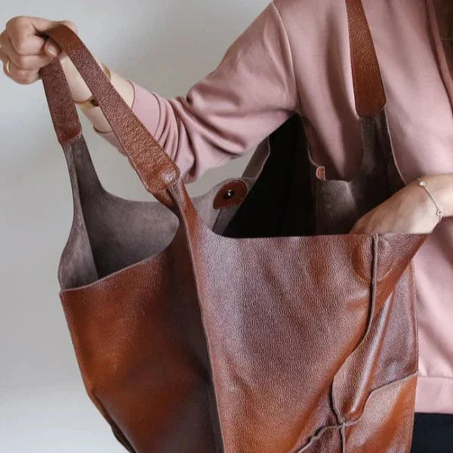 Borsa shopper in pelle marrone, ampia e resistente, indossata da una persona in maglia rosa. Design elegante, ideale per shopping e uso quotidiano.