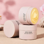 Crema viso pre-trucco in barattolo rosa, texture cremosa gialla, sfondo rosa sfocato. Ideale per idratazione e preparazione pelle.