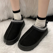 Scarpe invernali nere da donna, suola spessa antiscivolo, dettagli ricamati, indossate con calzini bianchi e neri su tappeto bianco.