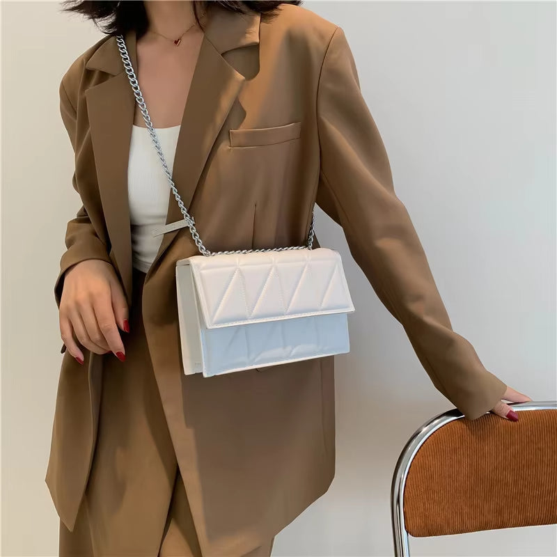 Donna con blazer marrone e borsa a tracolla bianca trapuntata, elegante e moderna, su sfondo neutro. Accessorio moda femminile di tendenza.
