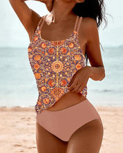 Donna in costume da bagno a due pezzi con top a fantasia floreale arancione e viola, su spiaggia estiva. Moda mare, abbigliamento donna, estate.