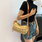 Borsa a tracolla trapuntata beige con manico in corda arancione, indossata da una donna in maglietta nera e shorts di jeans. Accessorio moda casual.