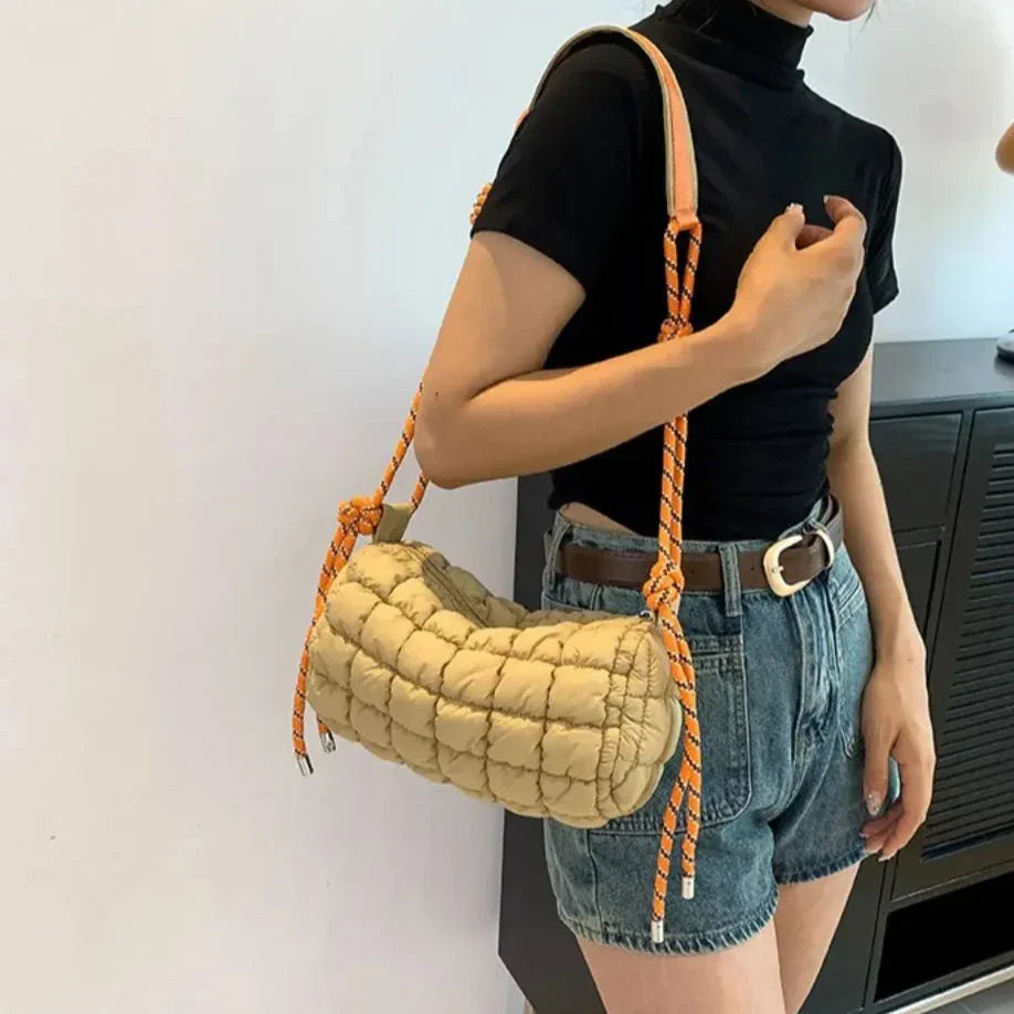 Borsa a tracolla trapuntata beige con manico in corda arancione, indossata da una donna in maglietta nera e shorts di jeans. Accessorio moda casual.