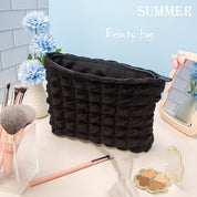 Borsa trucco nera in tessuto trapuntato su tavolo da trucco, circondata da pennelli, fiori blu e specchio. Accessorio essenziale per cosmetici.