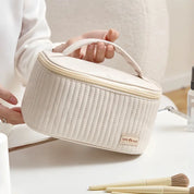Borsa cosmetica beige trapuntata con manico, design elegante e compatto, ideale per organizzare trucchi e accessori da viaggio.