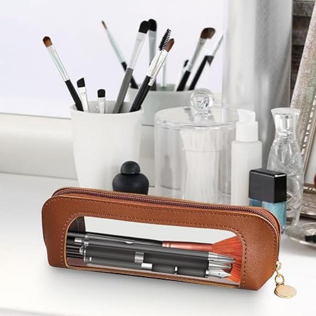 Astuccio trasparente in pelle marrone su tavolo da trucco, contenente pennelli e cosmetici. Accessorio elegante per organizzare il make-up.