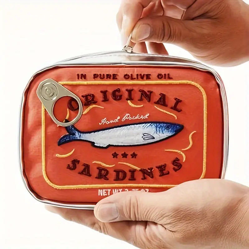 Due mani tengono una scatola di sardine in olio d'oliva, confezione rossa con illustrazione di pesce e scritta "Original Sardines".