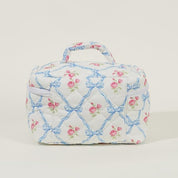 Borsa da toilette trapuntata con motivo floreale rosa e fiocchi blu, manico superiore, design elegante, ideale per viaggi e organizzazione cosmetici.