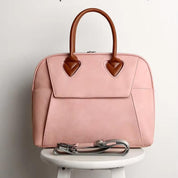 Borsa a mano rosa in pelle con manici marroni, design elegante, perfetta per moda femminile, accessorio di tendenza, su sgabello bianco.